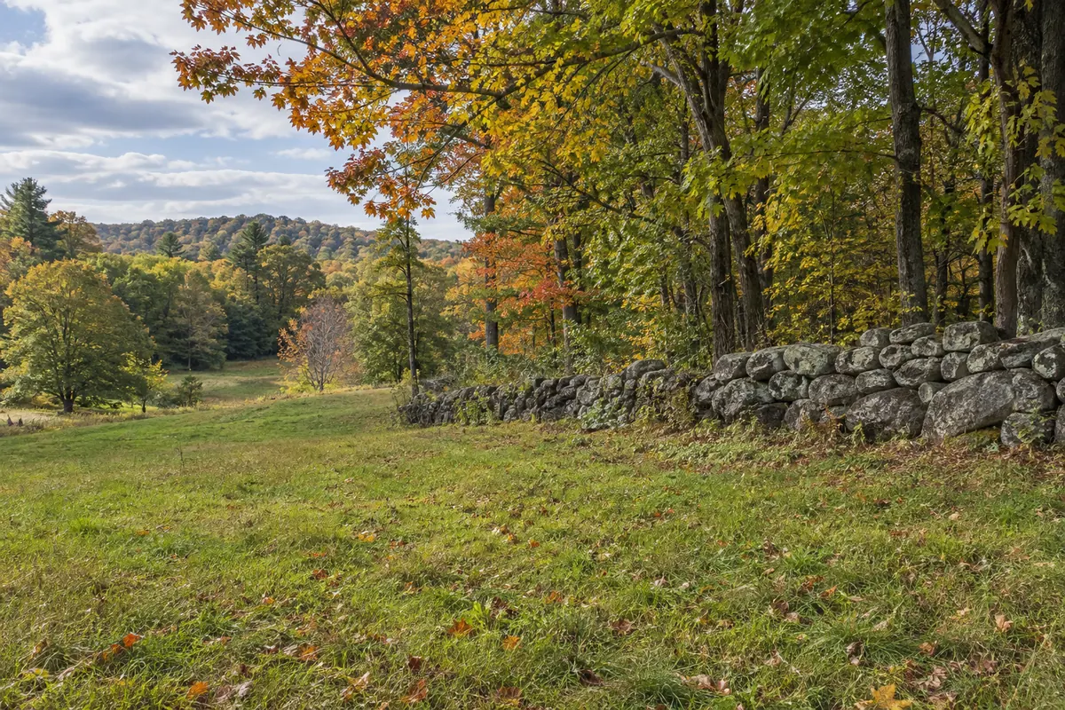 An old stone wall beside a clearing and autumn woods