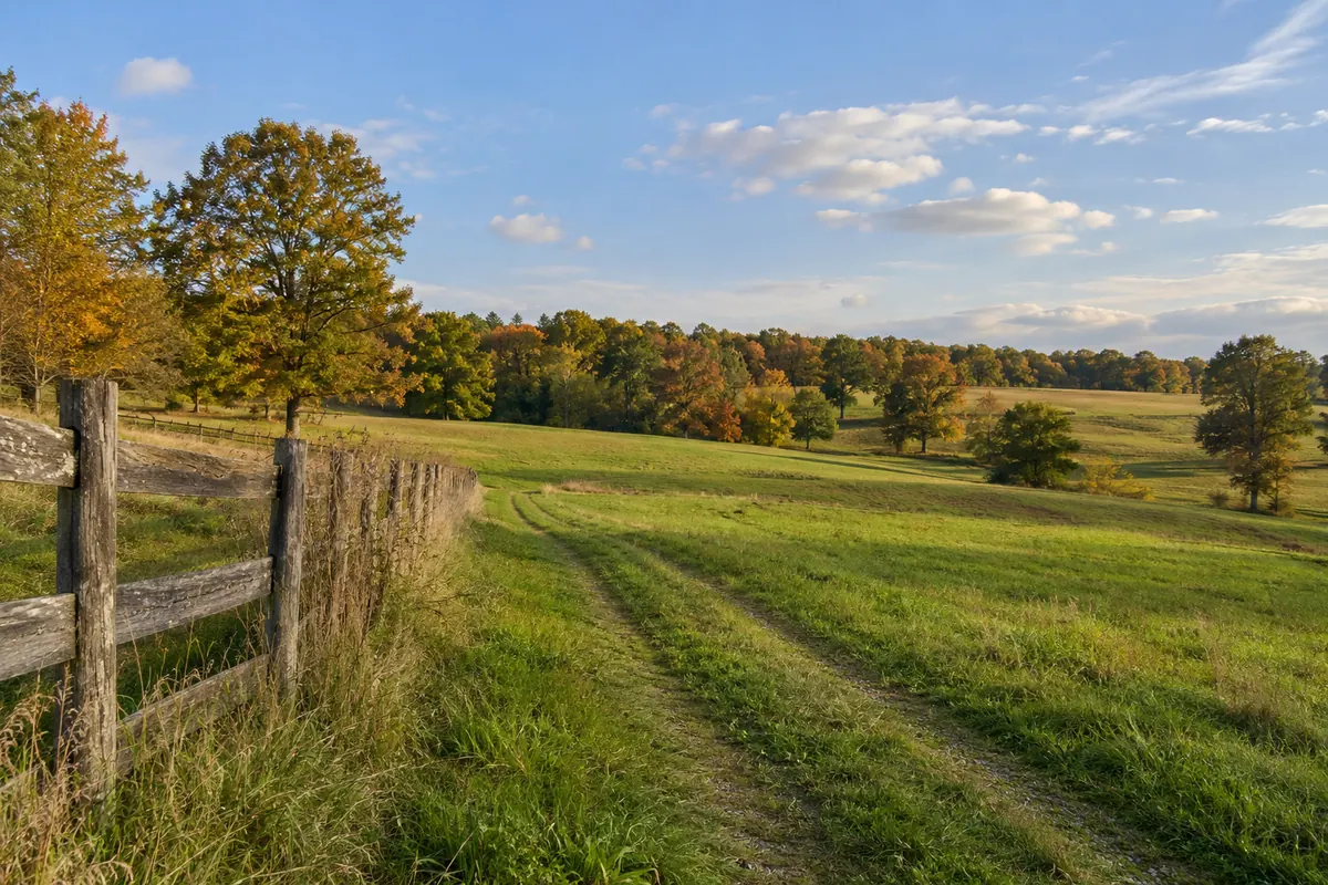 A wooden fence beside rolling fields and autumn trees