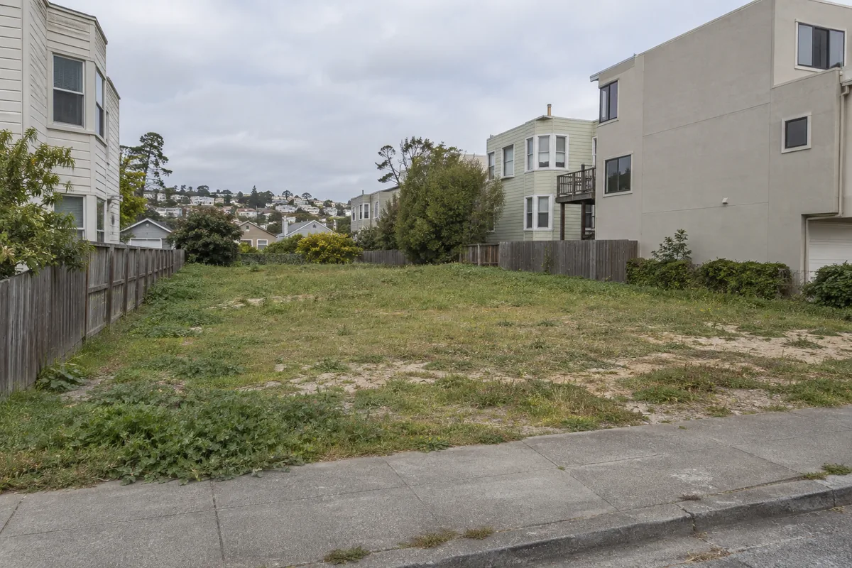 A grassy vacant lot between neighboring homes on an overcast day